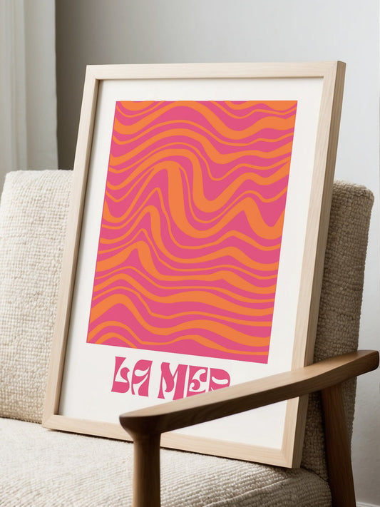 Abstract wave art print with flowing pink and orange wavy bands, La Mer text, displayed in modern living room setting