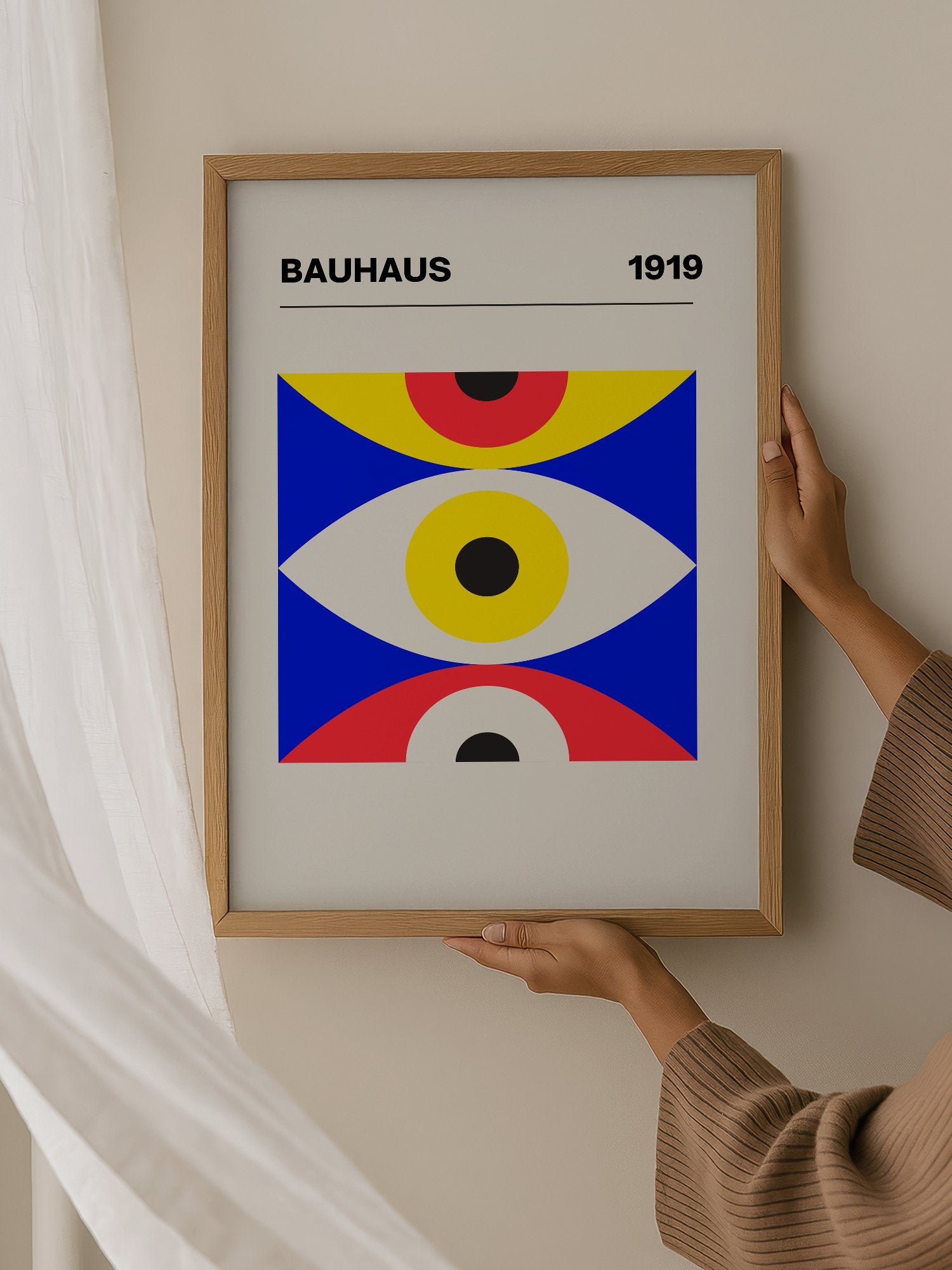 Bauhaus 1919 geometric poster with three stacked eye shapes in yellow red and, hanging in contemporary bedroom interior