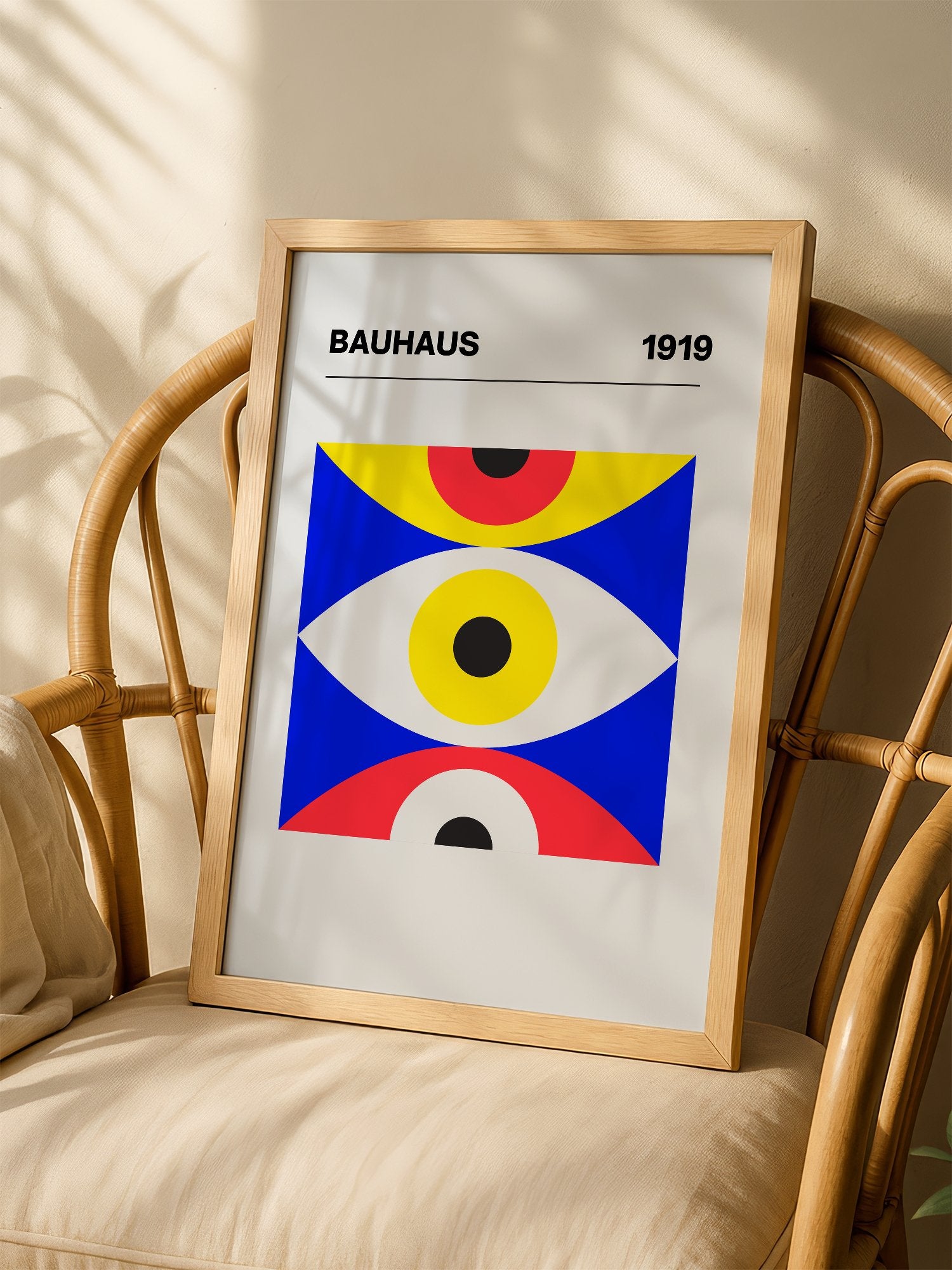 Bauhaus 1919 geometric poster with three stacked eye shapes in yellow red and, shown in minimalist home office space