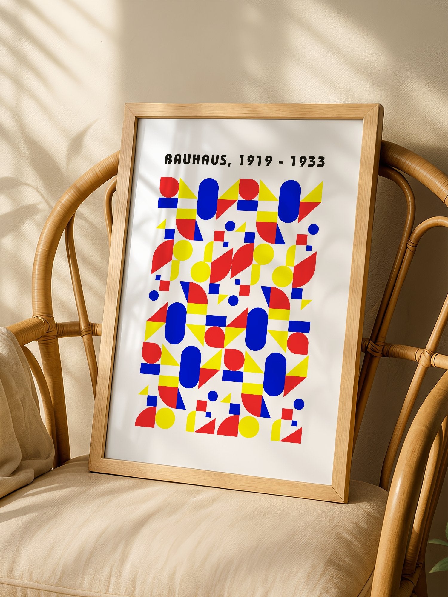 Bauhaus geometric poster with red circles, yellow triangles, and blue ovals in, shown in minimalist home office space