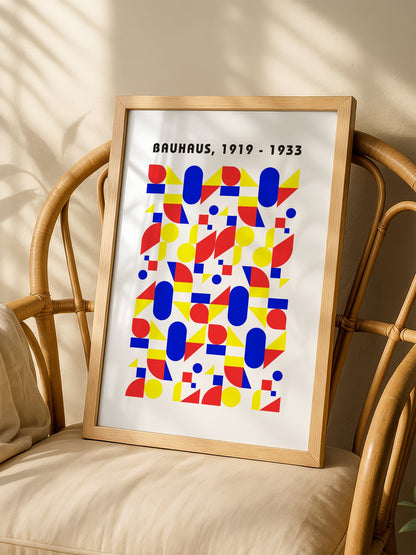 Bauhaus geometric poster with red circles, yellow triangles, and blue ovals in, shown in minimalist home office space