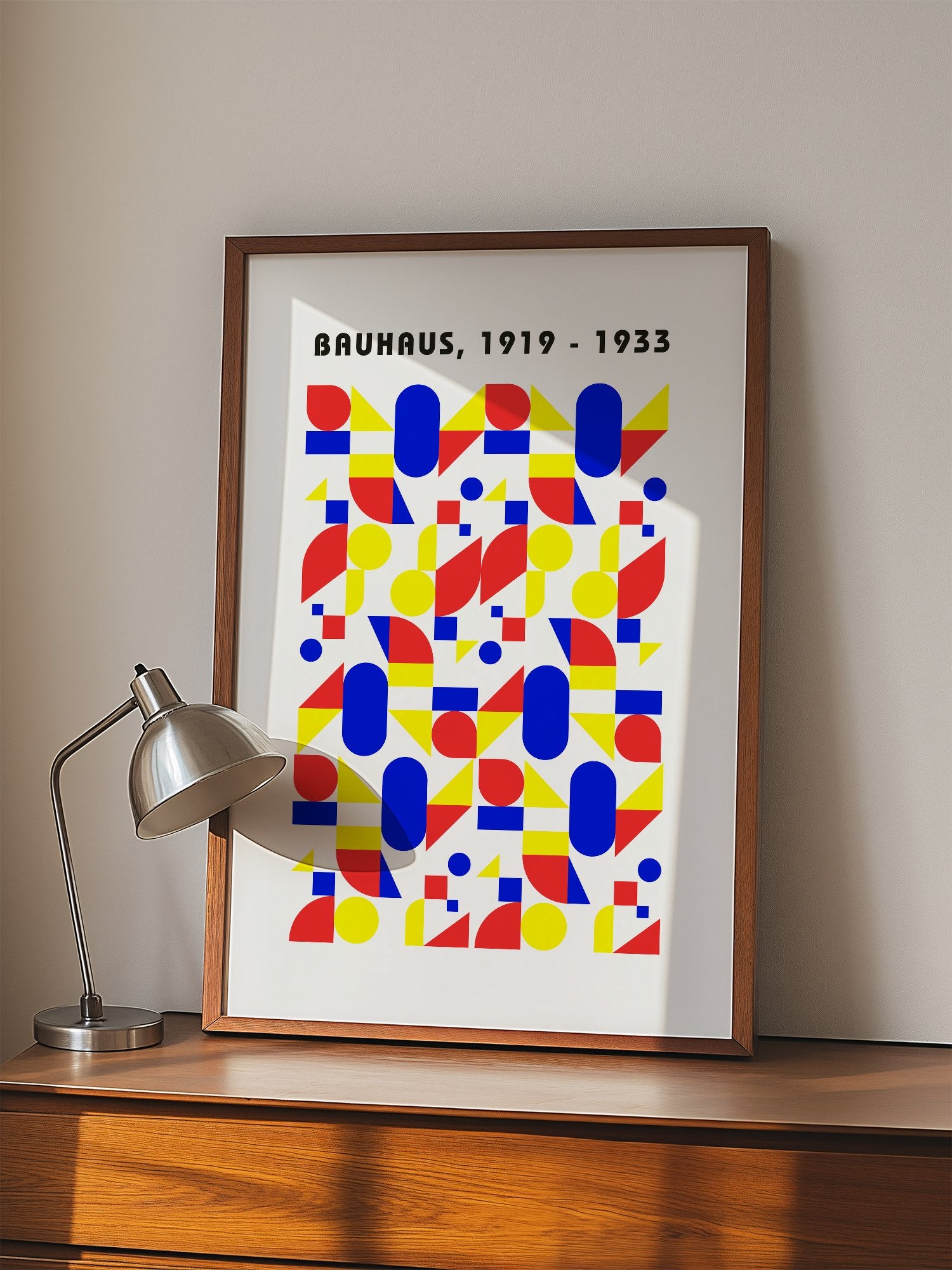 Bauhaus geometric poster with red circles, yellow triangles, and blue ovals in, displayed in modern living room setting