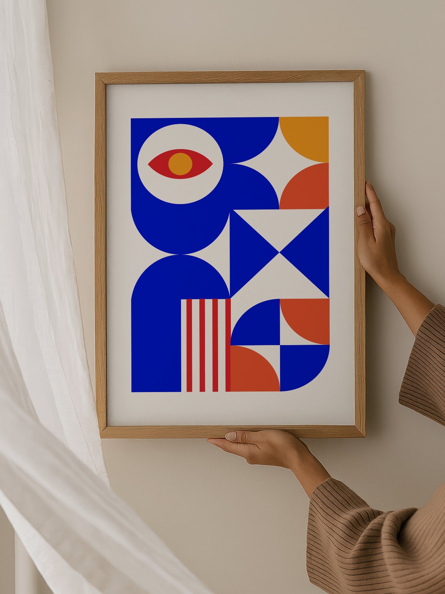 Geometric abstract art print with red eye motif, blue background, coral and, hanging in contemporary bedroom interior